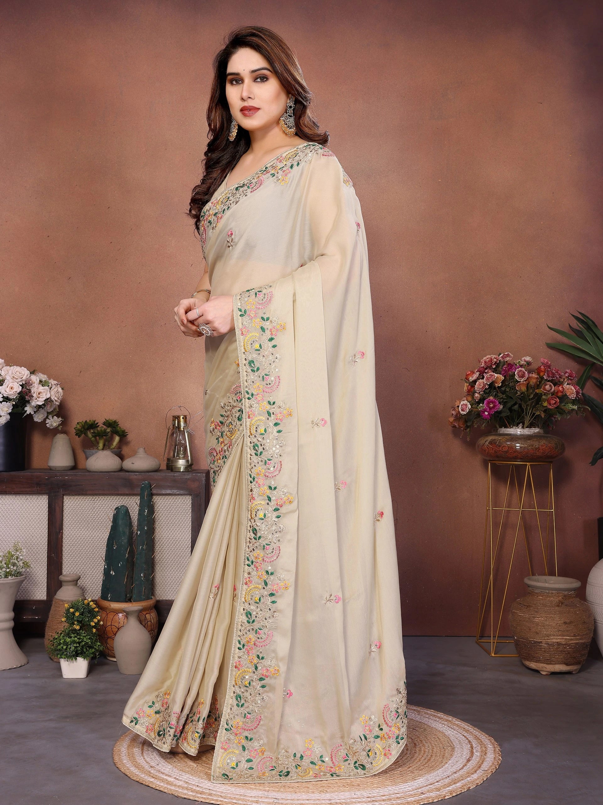 Woman wearing a beige saree with floral patterns in a decorated room.
